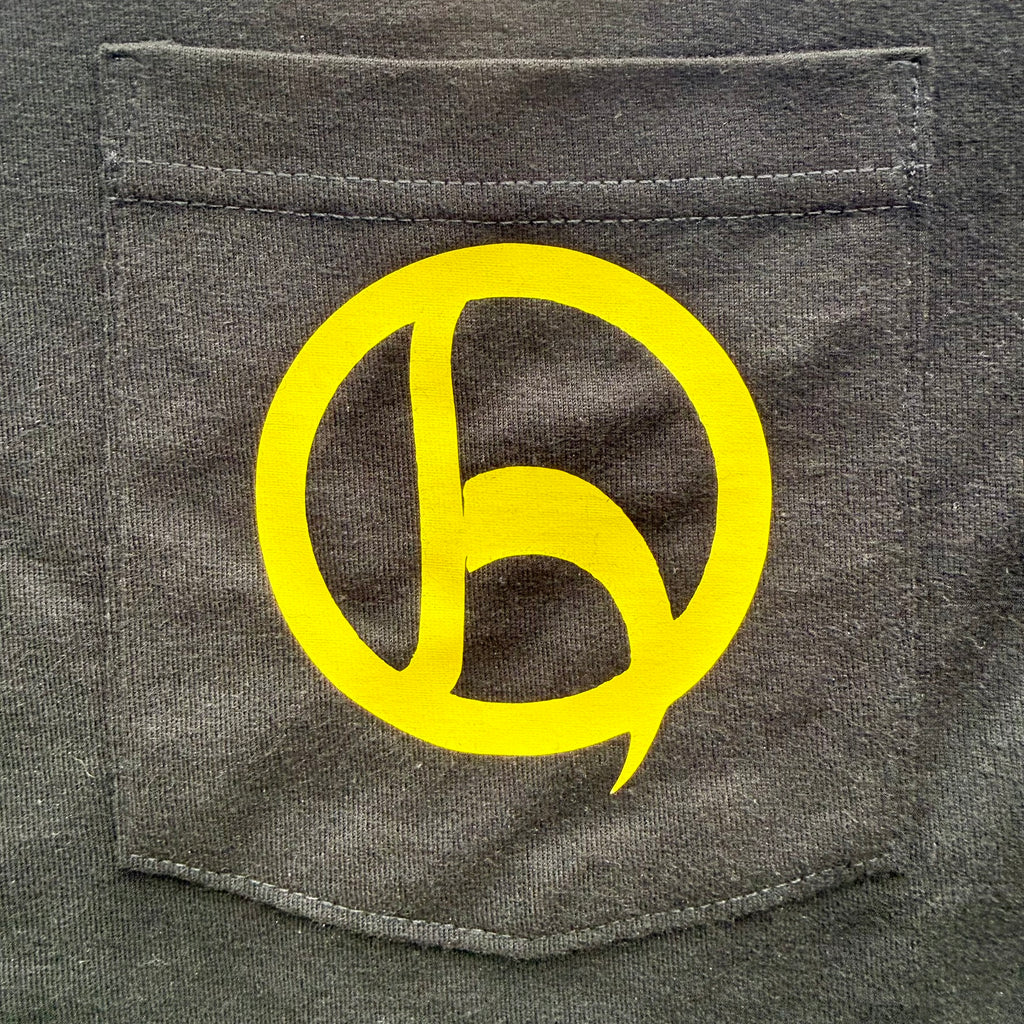 A close-up of a black pocket on a shirt, featuring a large yellow graphic logo printed on the front pocket.