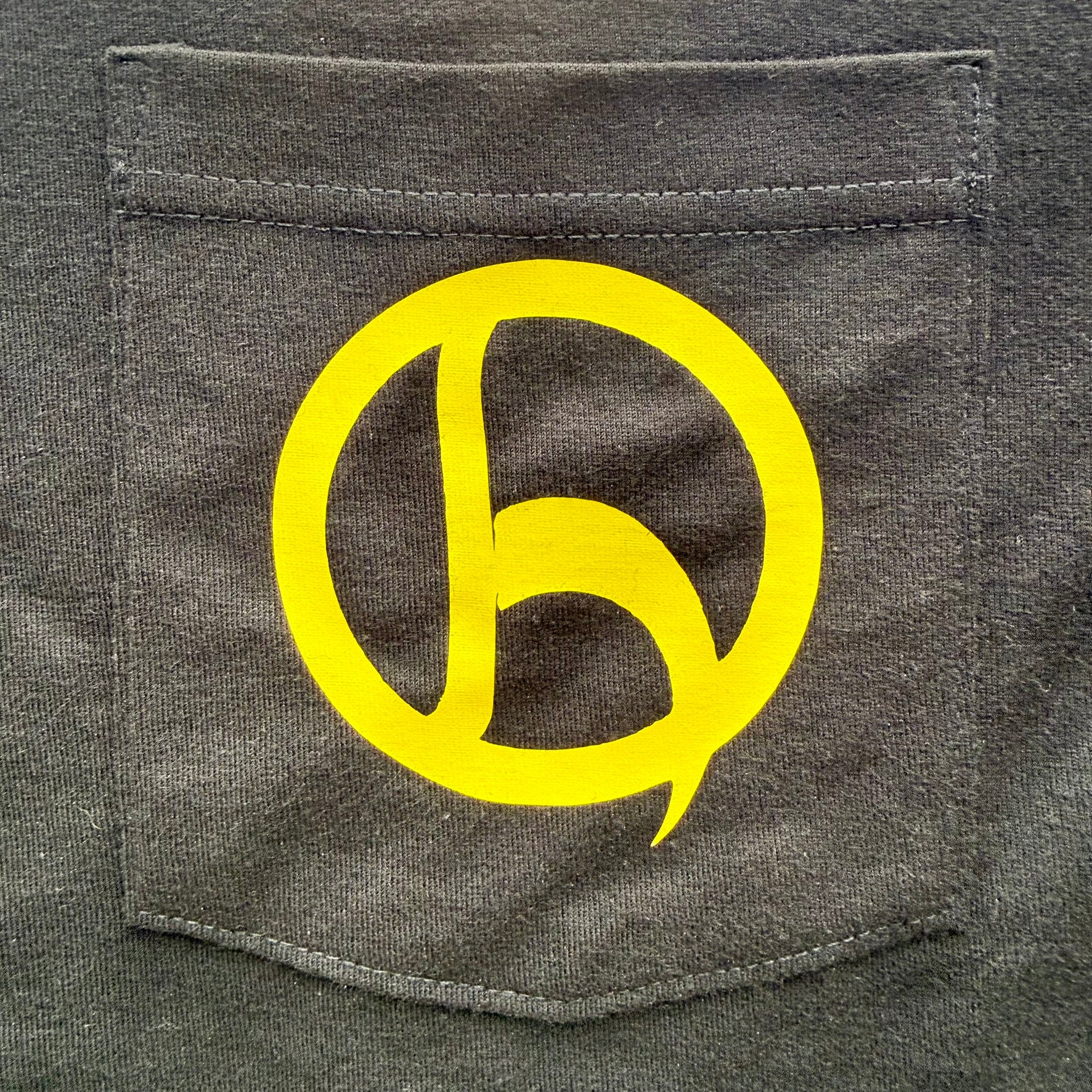A close-up of a black pocket on a shirt, featuring a large yellow graphic logo printed on the front pocket.